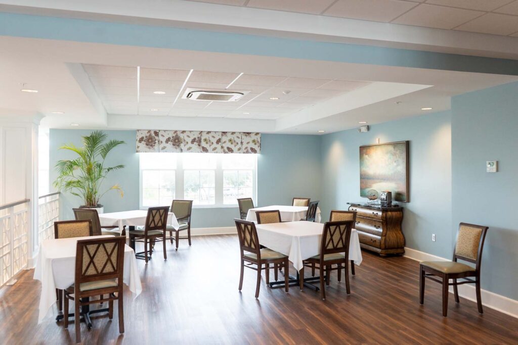 Interior image of The Arbors of Gulf Breeze dining room with 2-person and 4-person tables with white linens for senior living residents to enjoy meals together.