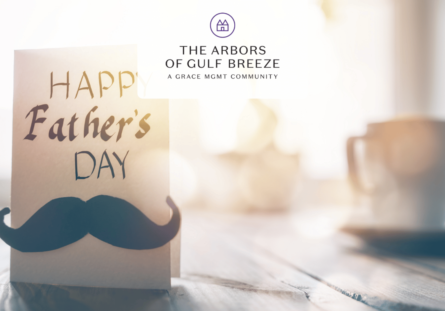 Card reading 'Happy Father's Day' with a blue mustache cutout on a wooden table; blurred background and a logo above.